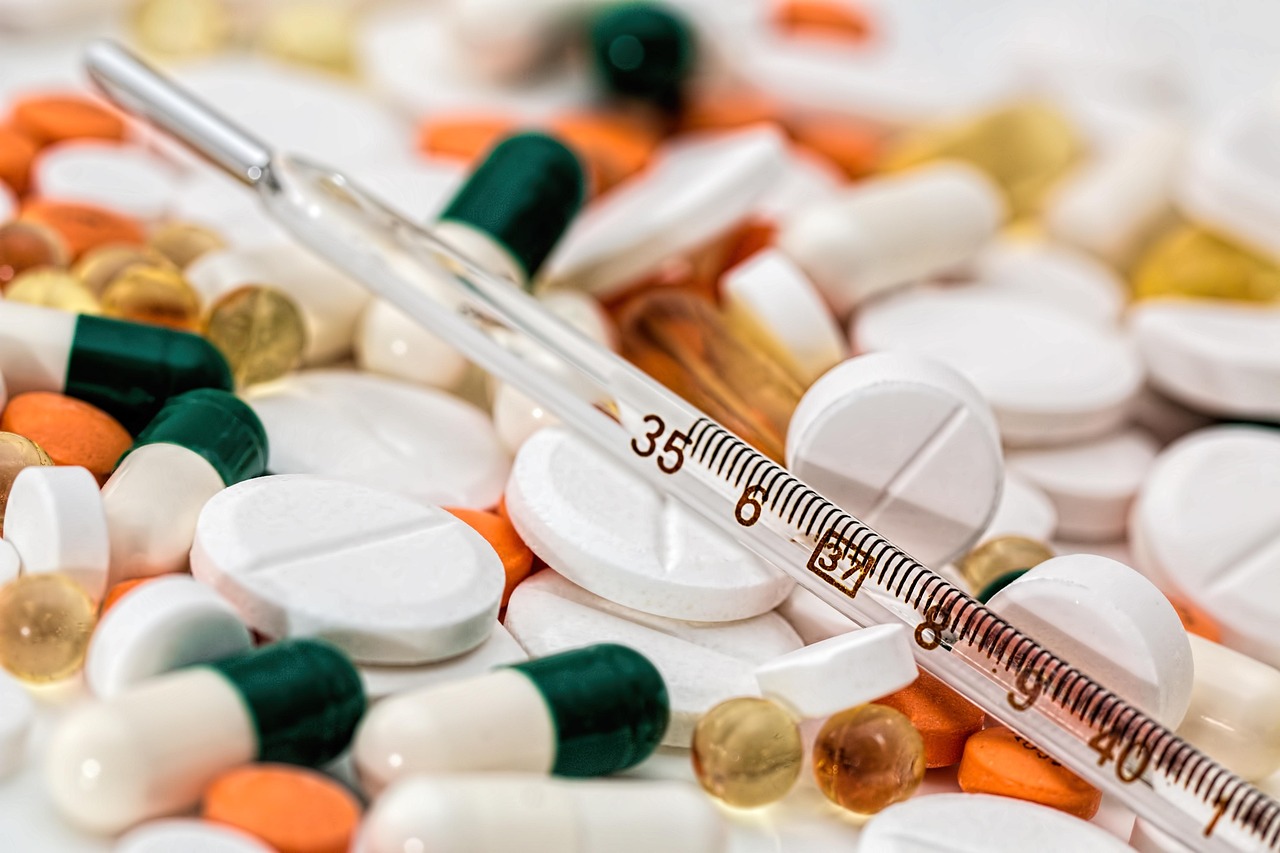 Ein Fieberthermometer liegt auf einem bunten Mix aus verschiedenen Tabletten und Kapseln.