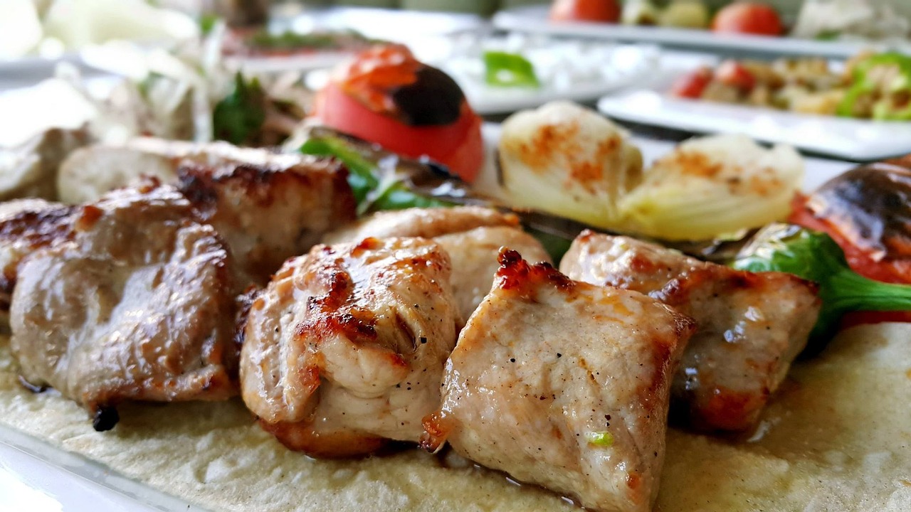 Nahaufnahme von saftigen, perfekt gegrillten Fleischstücken (wahrscheinlich Şiş Kebab), die leicht gebräunt sind und auf einem dünnen Fladenbrot liegen. Im Hintergrund sind gegrillte Zwiebeln, Tomaten und Paprika zu erkennen, was die Szenerie für 'Am lodernden Feuer: Mein Guide für das authentische Ocakbaşı-Erlebnis' perfekt untermalt und die herzhafte türkische Grillkultur hervorhebt.