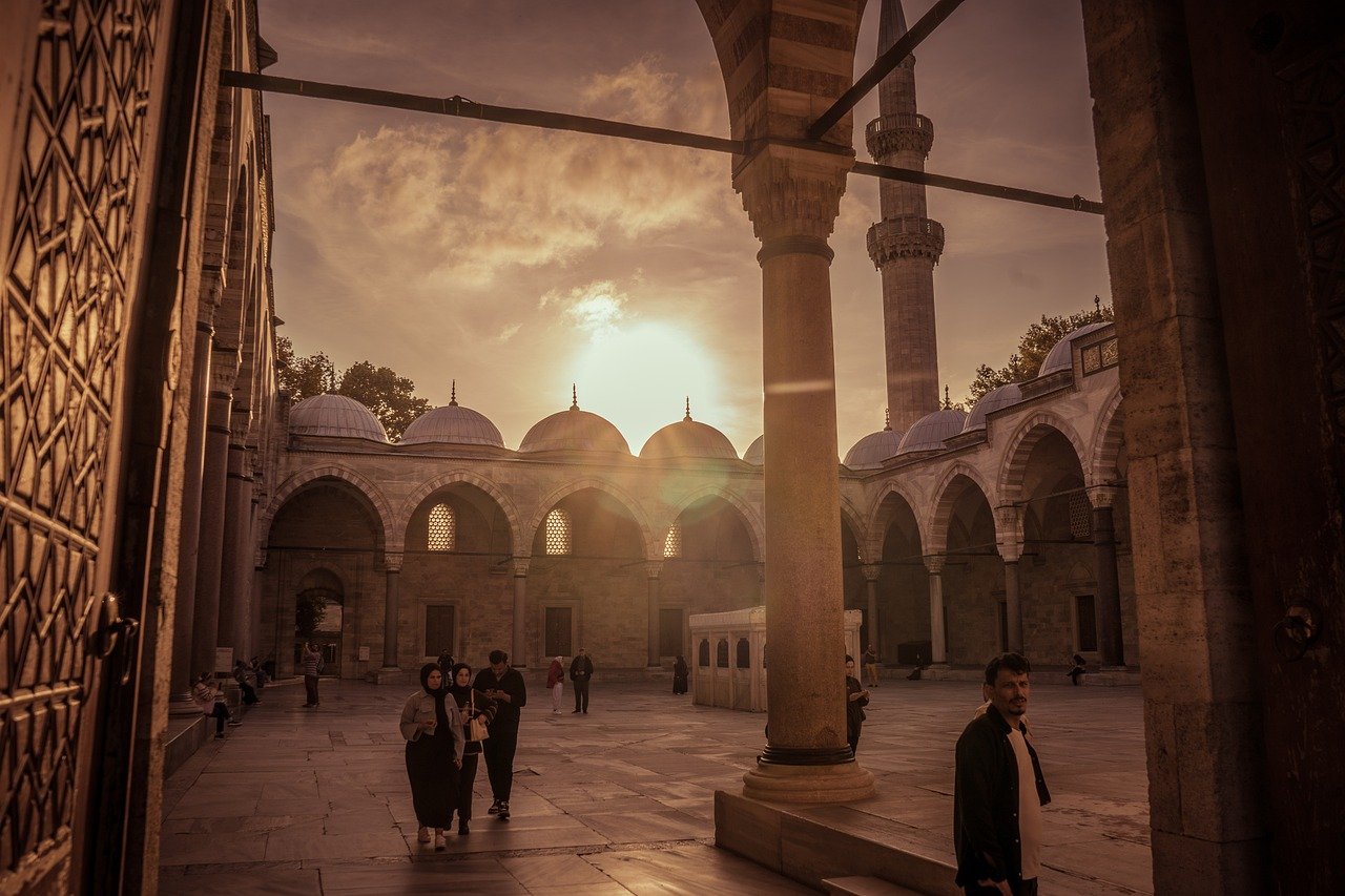 Menschen spazieren im warmen Abendlicht durch den prachtvollen Innenhof einer Istanbuler Moschee.