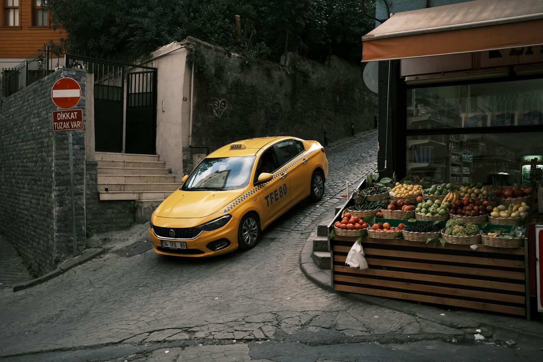 Ein gelbes Taxi manövriert durch eine enge Gasse vorbei an einem Obststand in Istanbul.