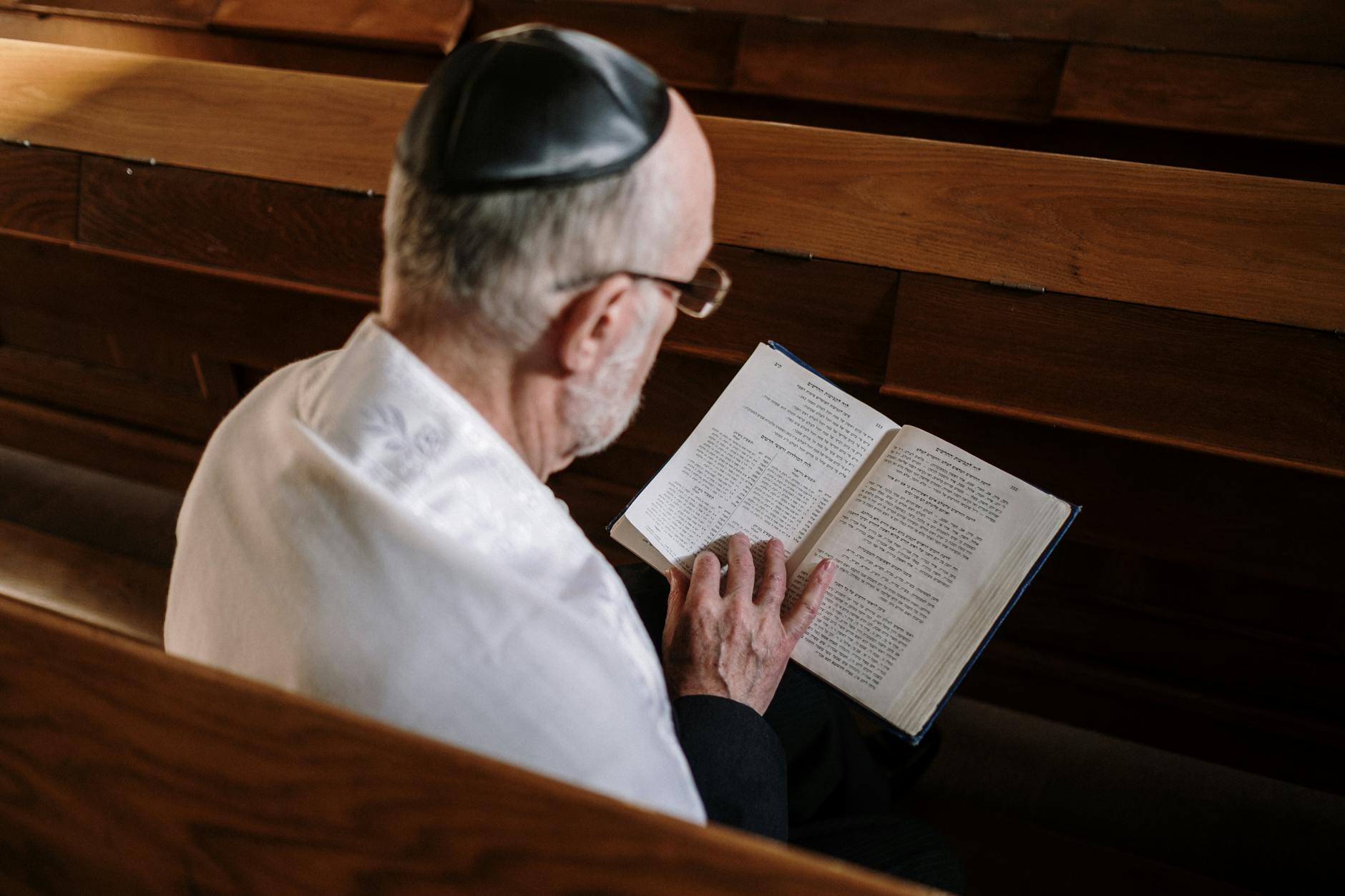 Ein älterer Mann mit Kippa liest aufmerksam in einem hebräischen Gebetbuch in der Synagoge.