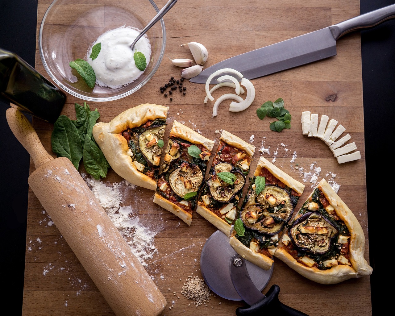 Aufgeschnittene Pide mit Auberginen und Schafskäse auf einem rustikalen Holzbrett angerichtet.