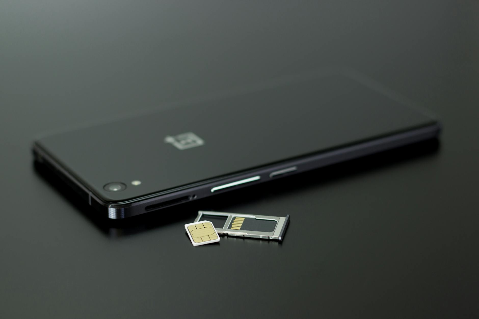 Ein schwarzes Smartphone liegt neben seinem geöffneten SIM-Karten-Halter.