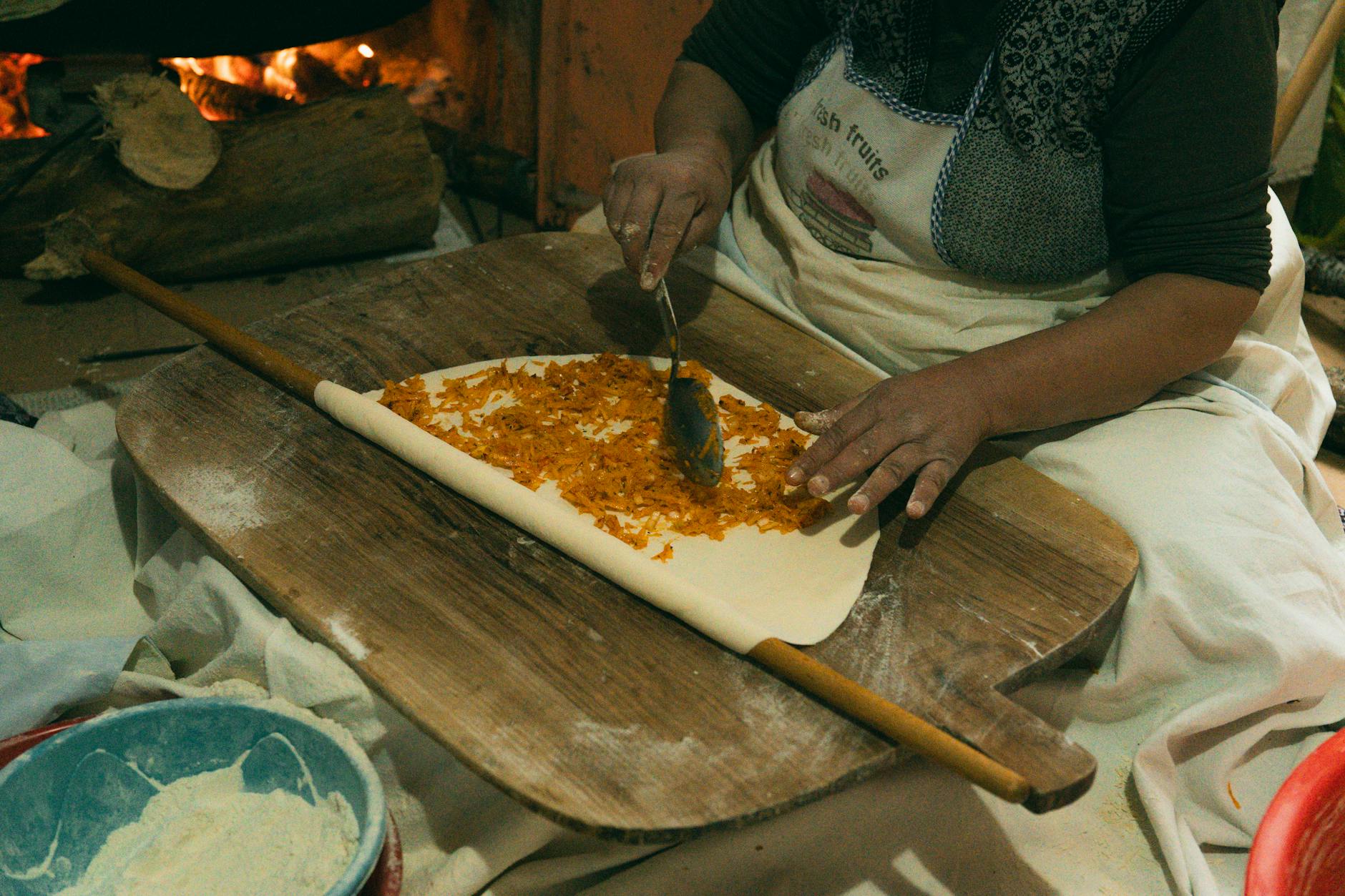 Eine Frau bereitet traditionelles türkisches Börek auf einem Holzbrett am Feuer zu.