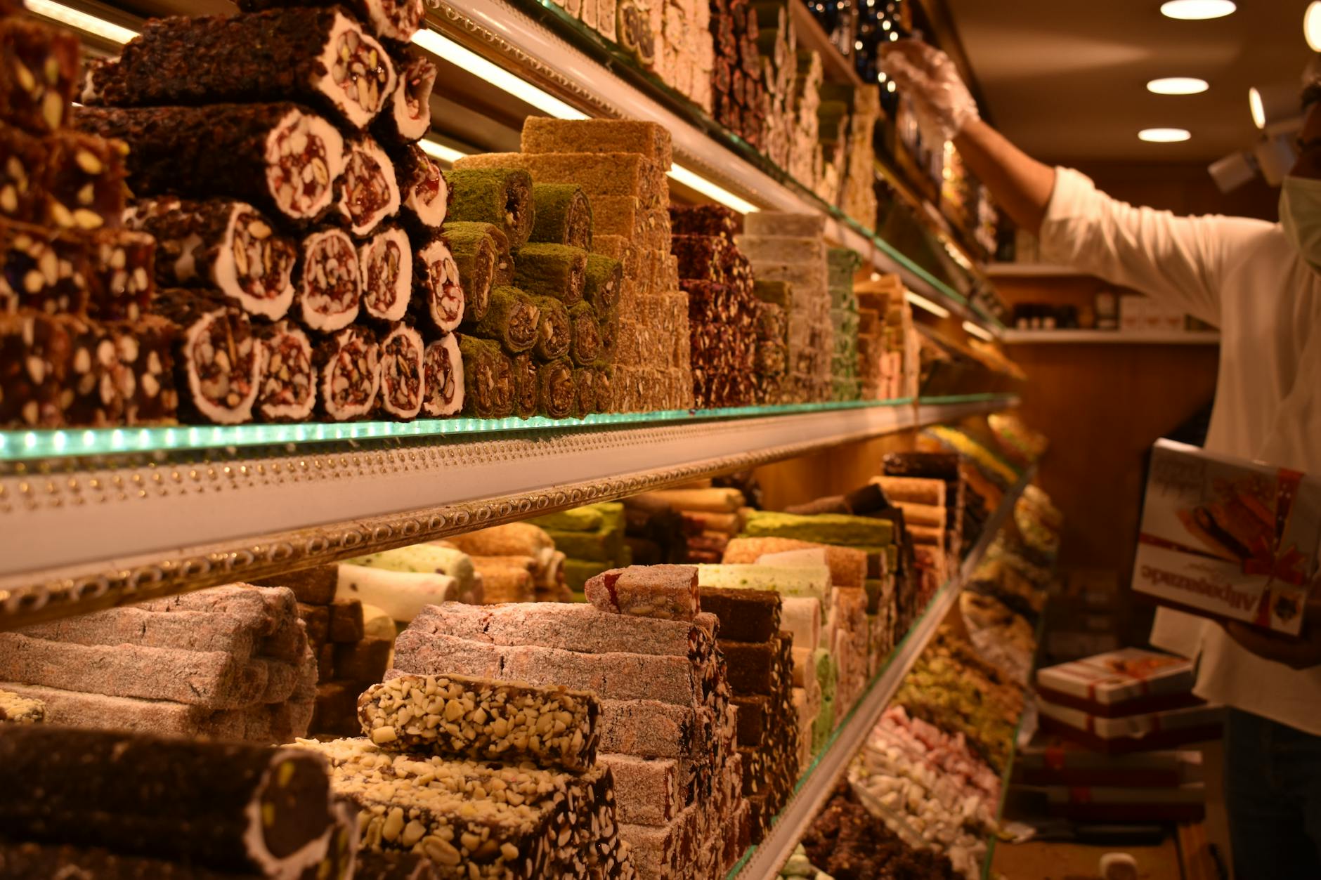 Reichhaltige Auswahl an verschiedenen Sorten türkischen Lokums (Turkish Delight) in einem Geschäft in Istanbul, mit einem Verkäufer im Hintergrund.
